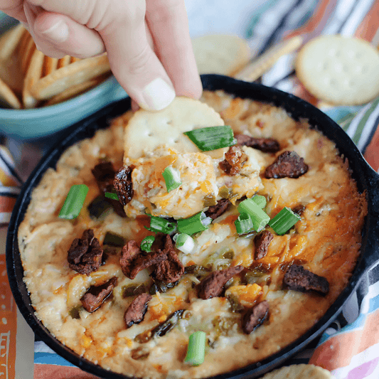 Creamy vegan snack dip topped with plant-based jerky, green onions, and served with crackers, perfect for flavorful and savory snacking