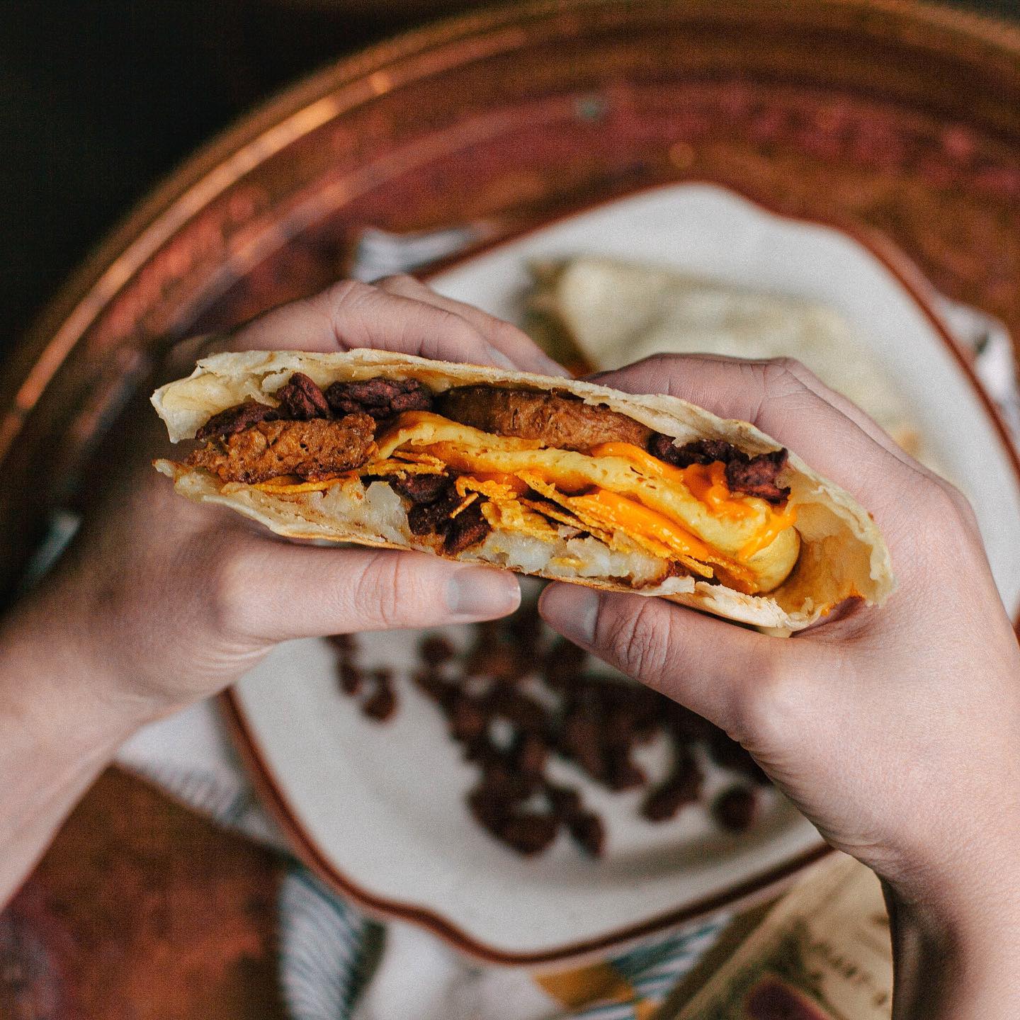 Hands holding a breakfast burrito filled with 'It’s Jerky Y’all,' highlighting one of the best vegan snacks for plant-based eating.