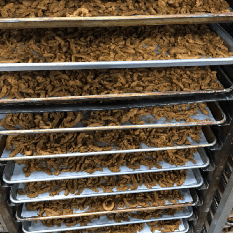 Racks filled with trays of plant-based jerky strips in the process of being prepared or dried, showcasing production in a commercial kitchen setting.