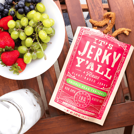 A bag of "It's Jerky Y’all" Prickly Pear Teriyaki plant-based jerky displayed next to a fresh fruit bowl for a perfect snack pairing.