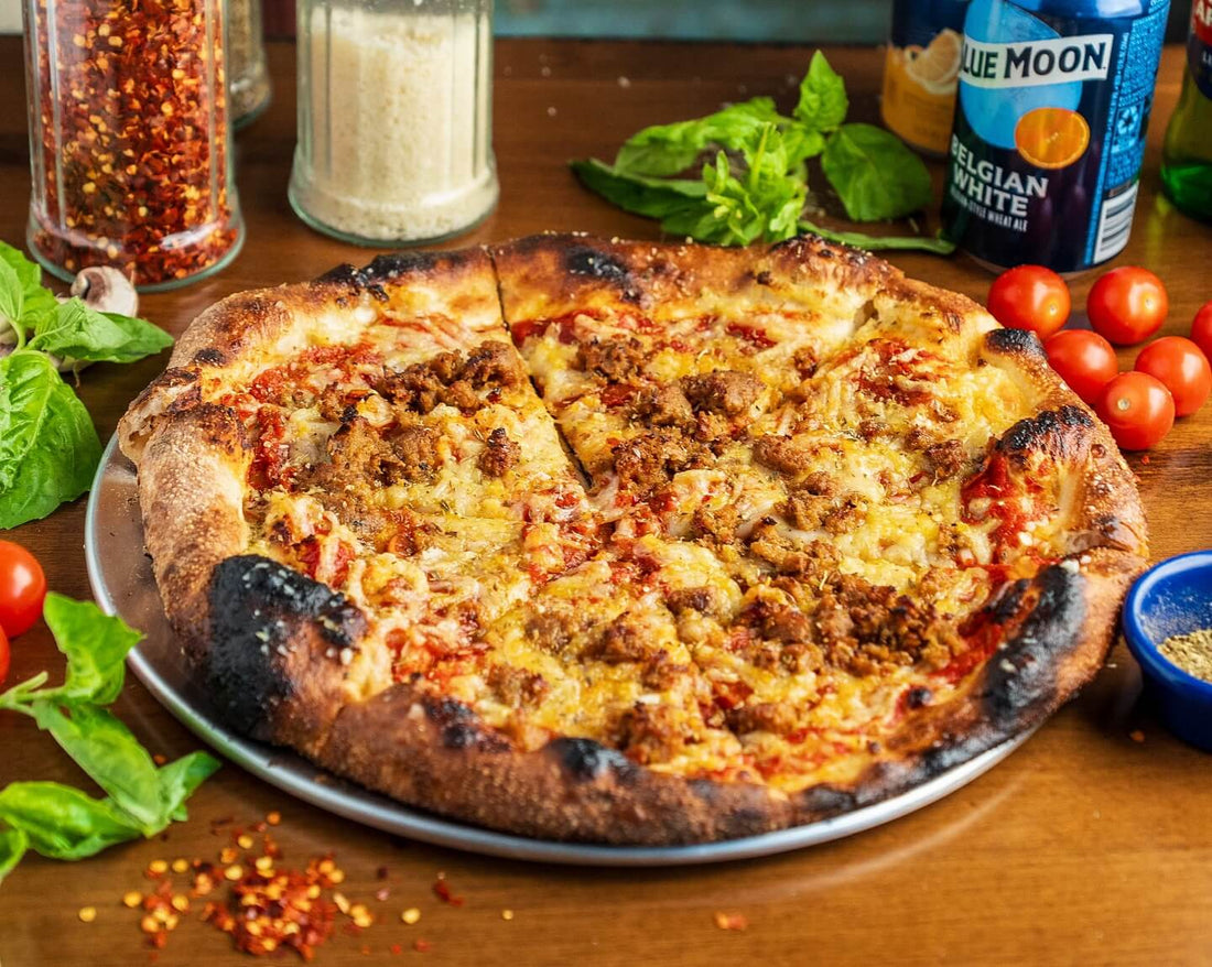 Wood-fired pizza topped with plant-based crumbles and melted cheese, surrounded by fresh basil, cherry tomatoes, and seasoning jars, showcasing a delicious option from plant-based pizzerias.