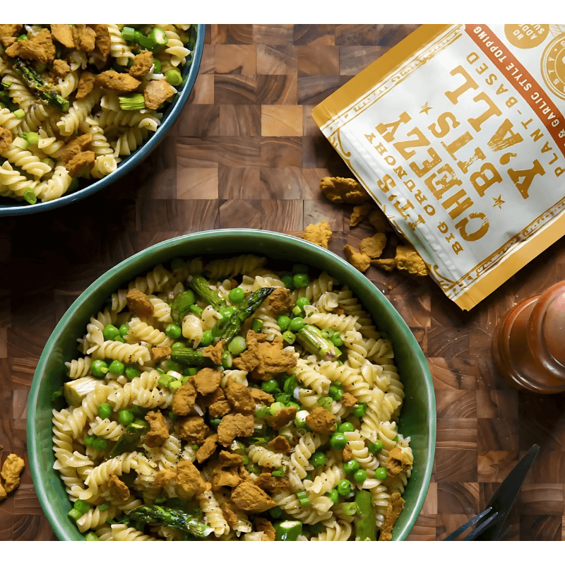 Pasta with asparagus, peas, and Big Crunchy Cheezy Bits sprinkled on top, served in a bowl for a delicious plant-based dish.