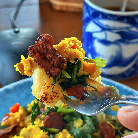 Forkful of a vibrant vegan breakfast scramble with crispy Bacony Bits, tofu, greens, and vegetables.