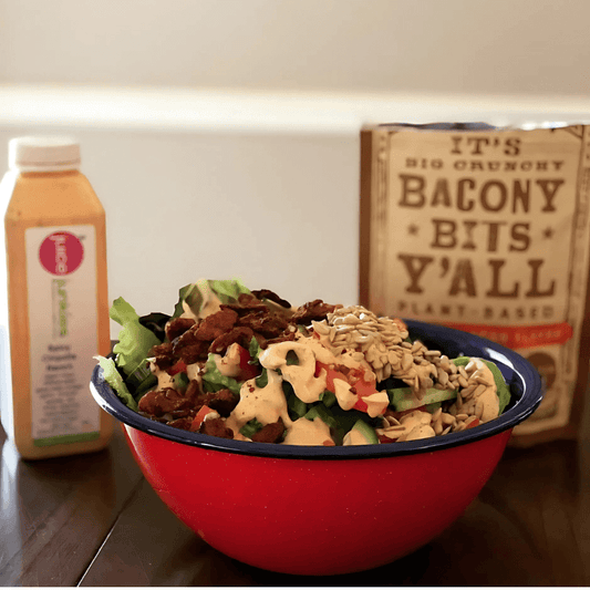 A colorful salad topped with sunflower seeds, plant-based bacony bits, and creamy dressing in a red bowl, showcasing 'Bacony Bits Y'all' as a plant-based protein snack option