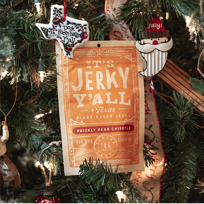 It's Jerky Y'all Prickly Pear Chipotle plant-based jerky, rich in plant-based proteins, hanging on a festive Christmas tree with Texas-themed ornaments.