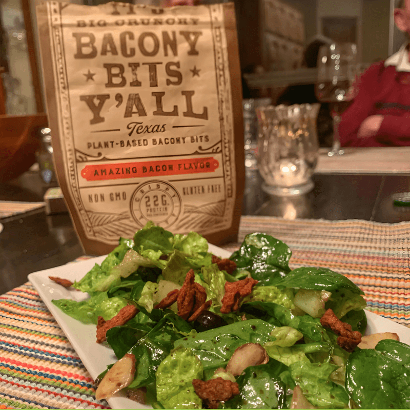 A fresh green salad topped with All Y'alls Foods' Big Crunchy Bacony Bits Y’all, a Texas plant-based protein snack offering a delicious bacon flavor, perfect for adding a savory crunch to vegetarian dishes.