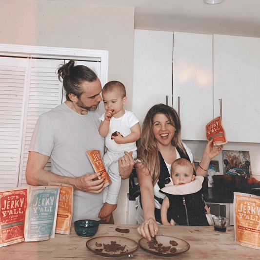 A happy family enjoys plant-based protein snacks from All Y'alls Foods' "It's Jerky Y'all" line, showcasing various flavors of the vegan jerky while gathered in their kitchen.