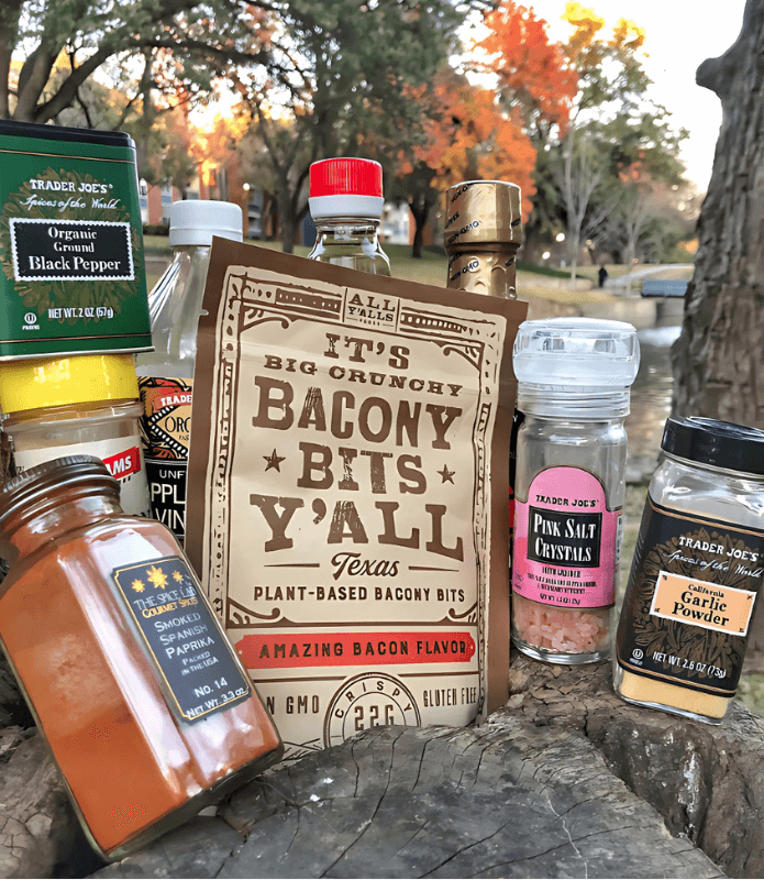 A rustic outdoor display of All Y’alls Foods’ plant-based Bacony Bits surrounded by Trader Joe’s spices, showcasing their versatile uses.