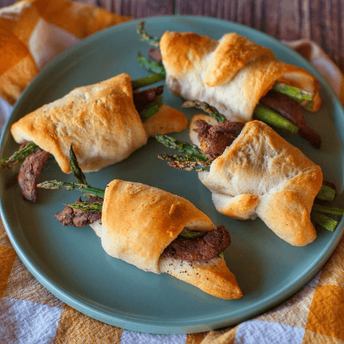 A plate of golden vegan crescent rolls stuffed with fresh asparagus and All Y’alls Foods' plant-based jerky, showcasing a tasty recipe from https://allyallsfoods.com/.