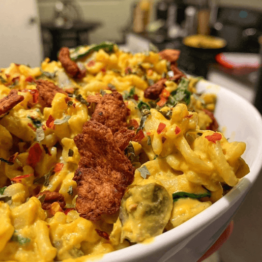  A creamy vegan mac and cheese topped with vibrant herbs and All Y’alls Foods plant-based jerky, adding bold flavor and texture to this savory dish.