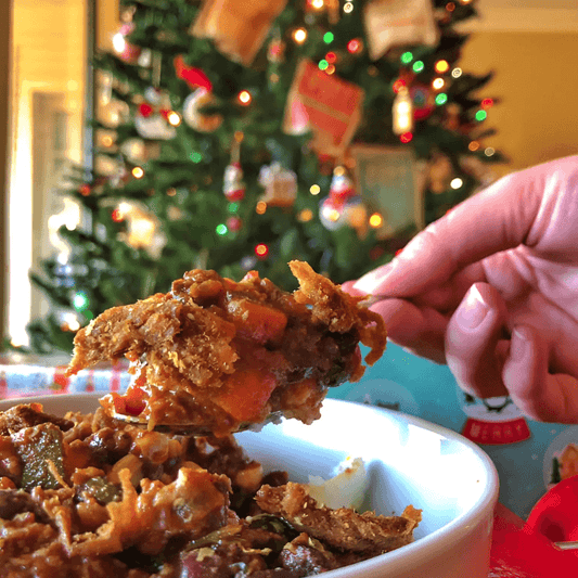 A spoonful of hearty, plant-based protein casserole filled with vibrant vegetables, set against a festive Christmas tree backdrop.