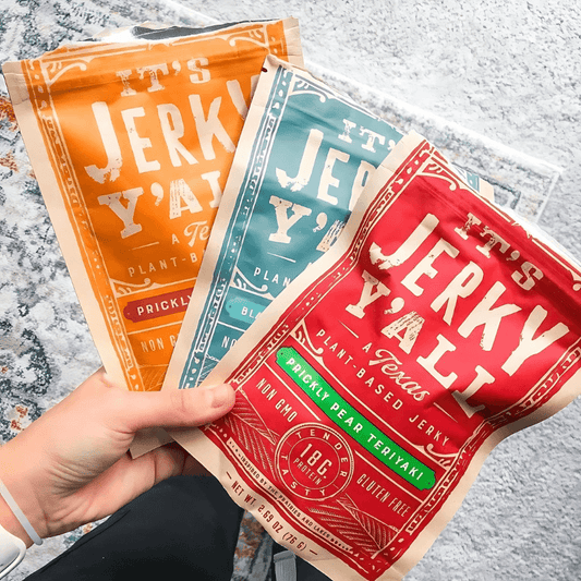 Hand holding a variety of colorful It's Jerky Y'all vegan jerky packs in Prickly Pear, Black Pepper & Sea Salt, and Prickly Pear Teriyaki flavors, showcasing plant-based, gluten-free snack options.