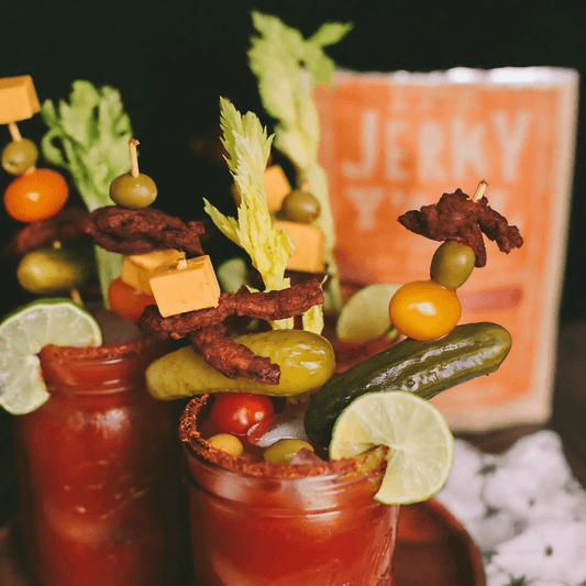 A vibrant Bloody Mary garnished with pickles, olives, cherry tomatoes, cheese cubes, and vegan jerky skewers for a unique and savory vegan twist on a classic cocktail.