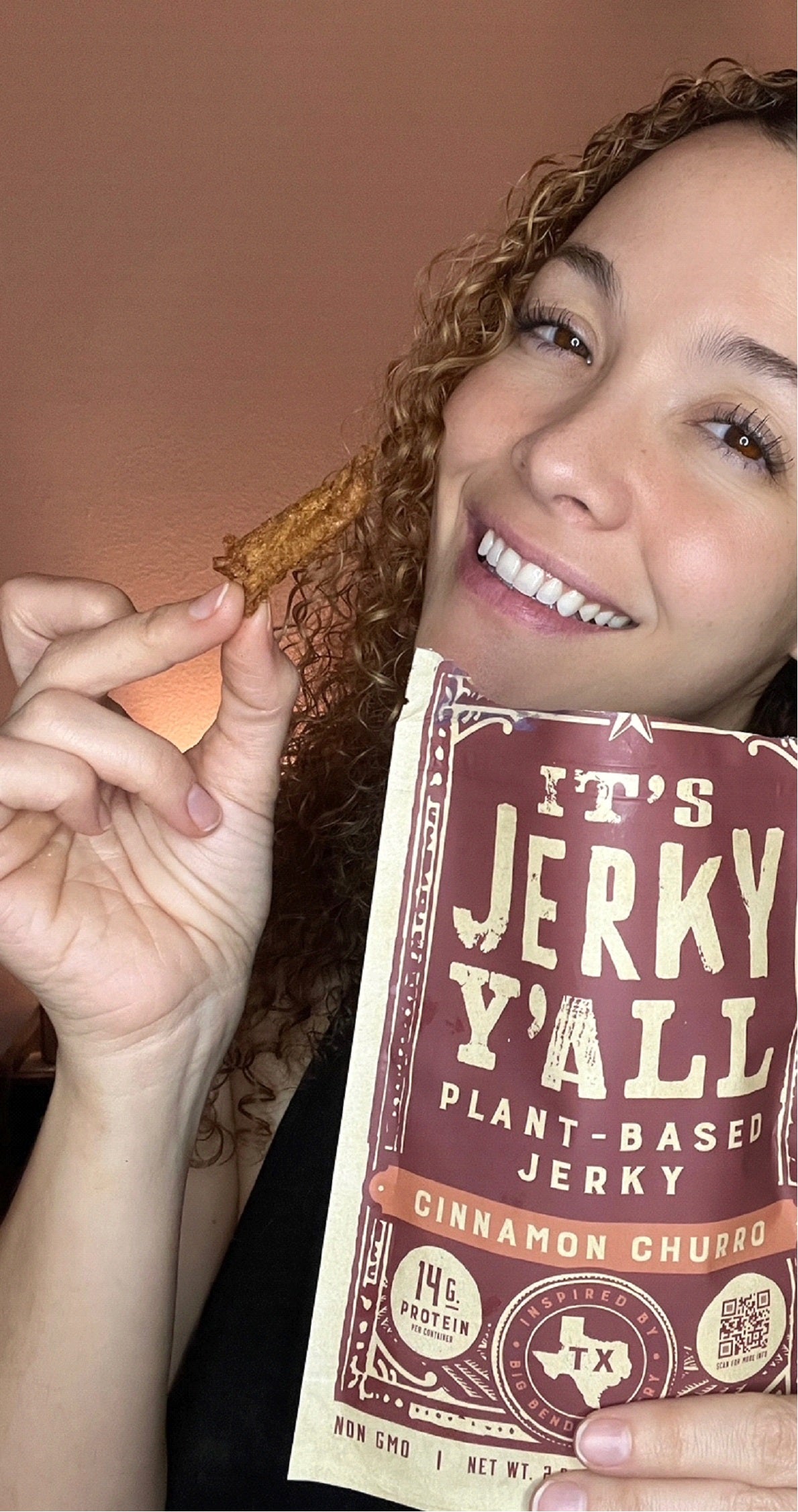 Smiling woman enjoying Cinnamon Churro plant-based jerky, a vegan-friendly and gluten-free snack, perfect for those seeking tasty vegan jerky and protein-packed plant-based treats.